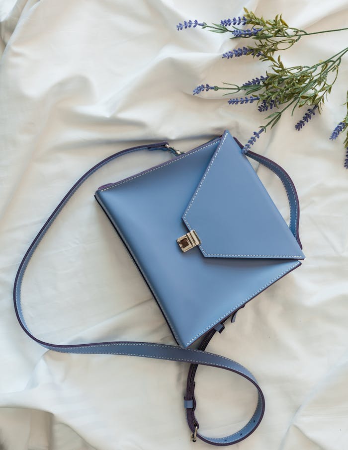 Stylish blue leather purse against a white background with lavender accents, perfect for chic fashion.